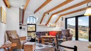 Un interior acogedor con vigas de madera, un sofá, sillas, una mesa y un amplio ventanal con vistas.