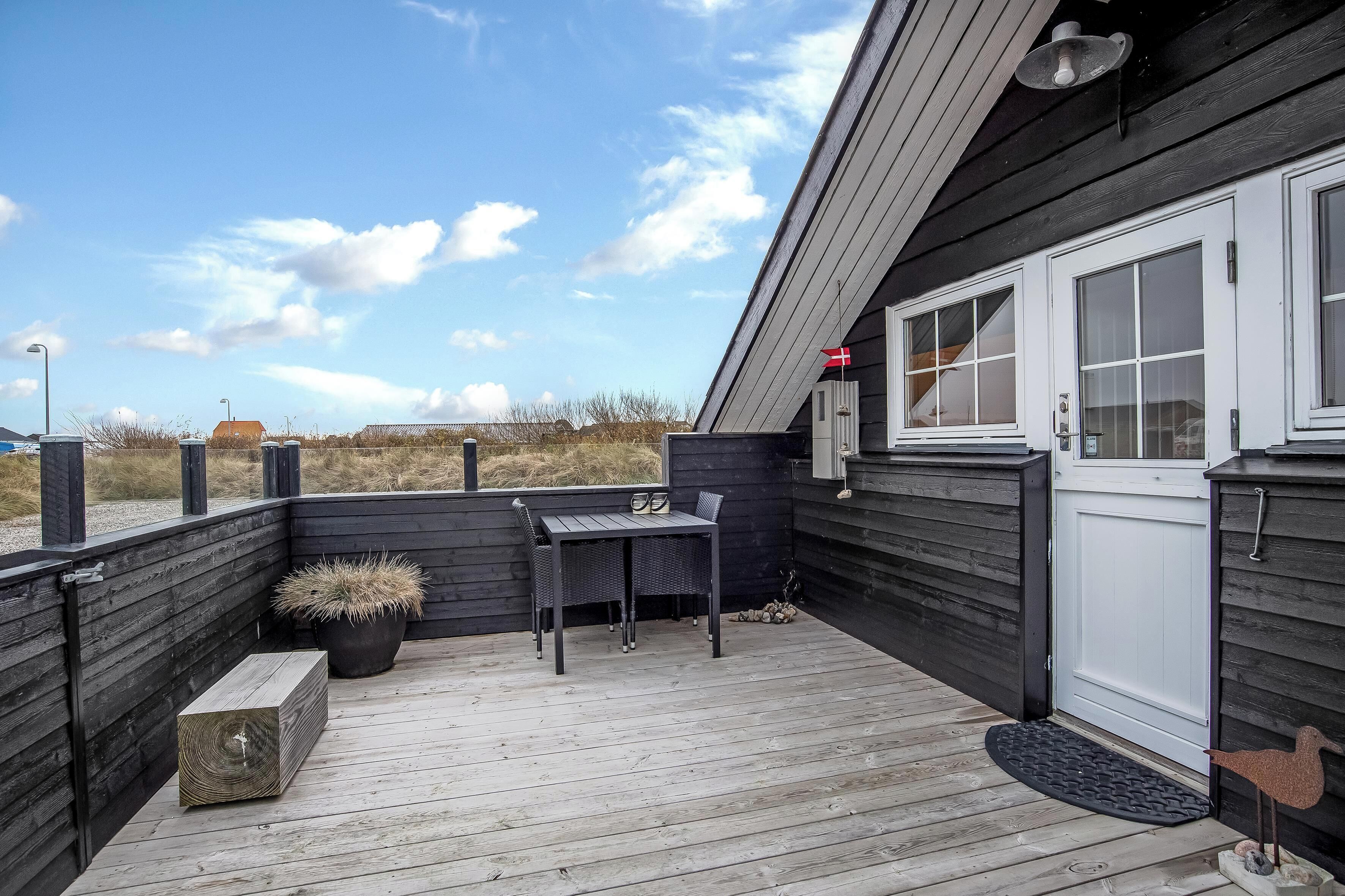 A wooden deck with a table and chairs, a potted plant, and a bird sculpture.