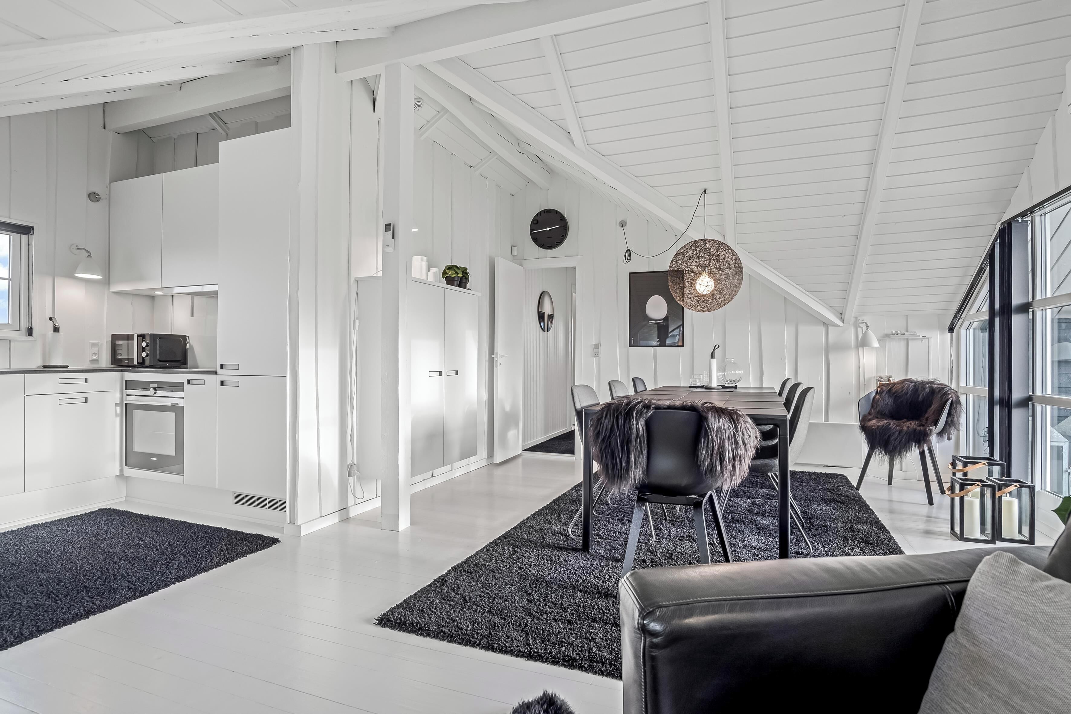 Eine moderne Küche mit weißen Schränken, ein Essbereich mit schwarzem Teppich und ein großes Fenster.