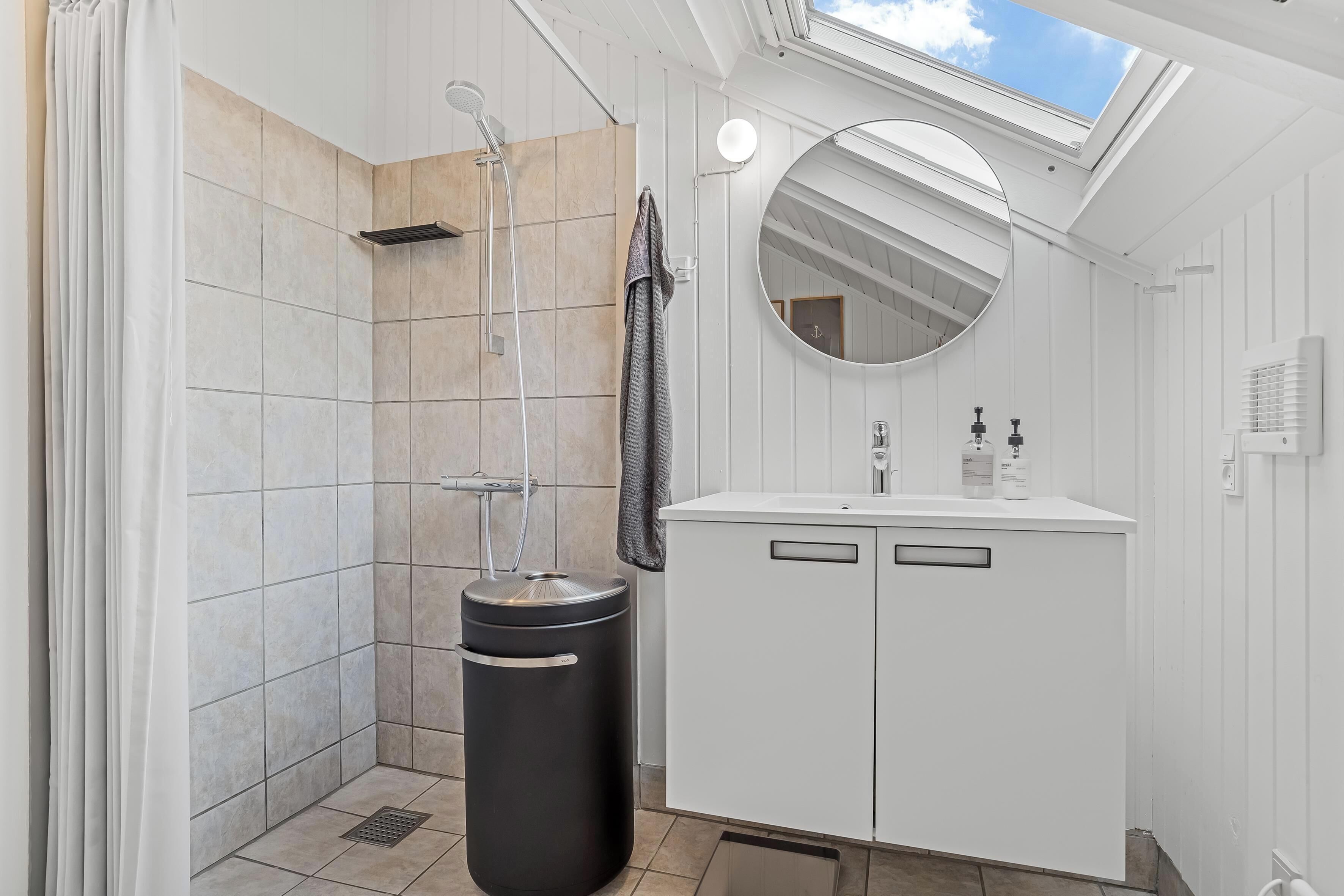 A bathroom with a shower, a sink, a mirror, and a skylight.