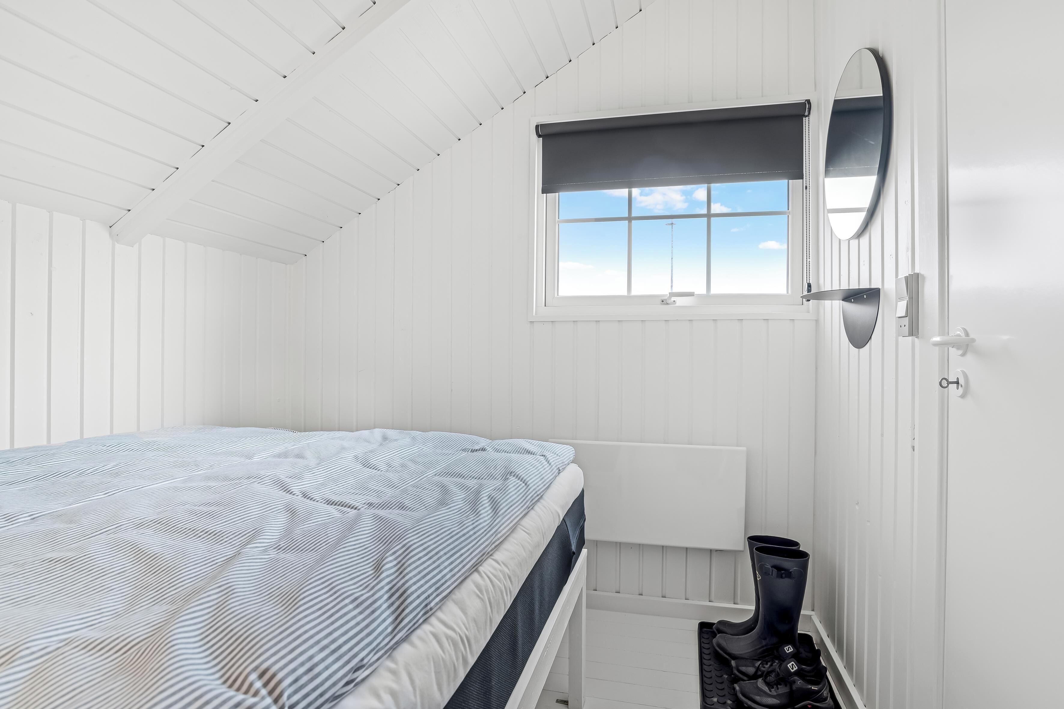 Une chambre avec un lit, une fenêtre donnant sur un beau paysage, un radiateur et une paire de bottes.