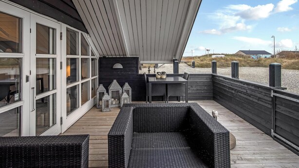 Un espacio al aire libre techado con piso de madera, muebles de mimbre y una mesa con sillas.