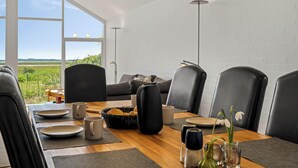Un coin repas avec vue sur l’extérieur, une table dressée avec des assiettes, des tasses et un panier de pain.