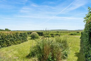A grassy landscape with a hedge, a path, and distant hills under a clear sky.