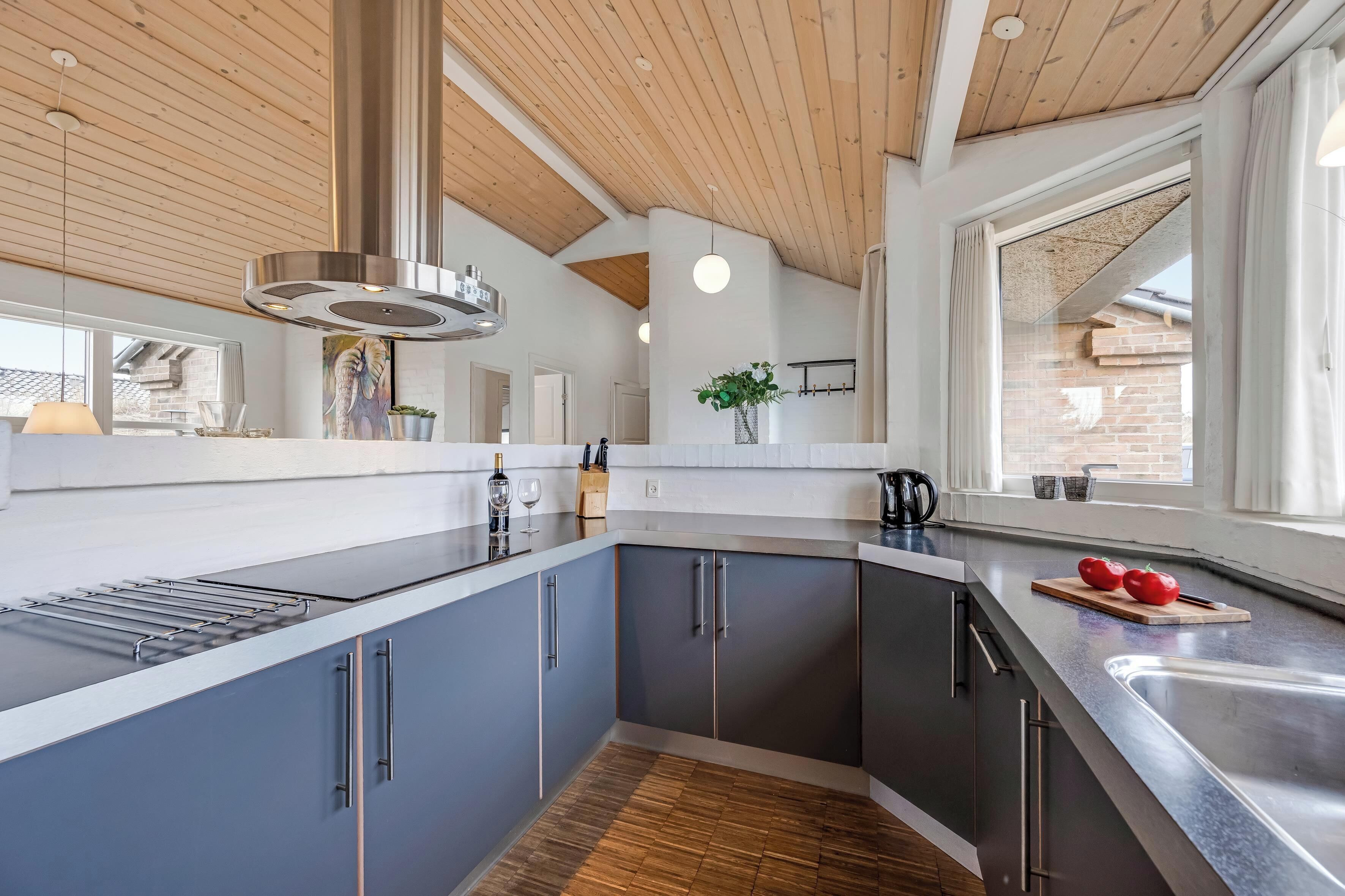 A modern kitchen with dark cabinets, a wooden ceiling, and a large window.