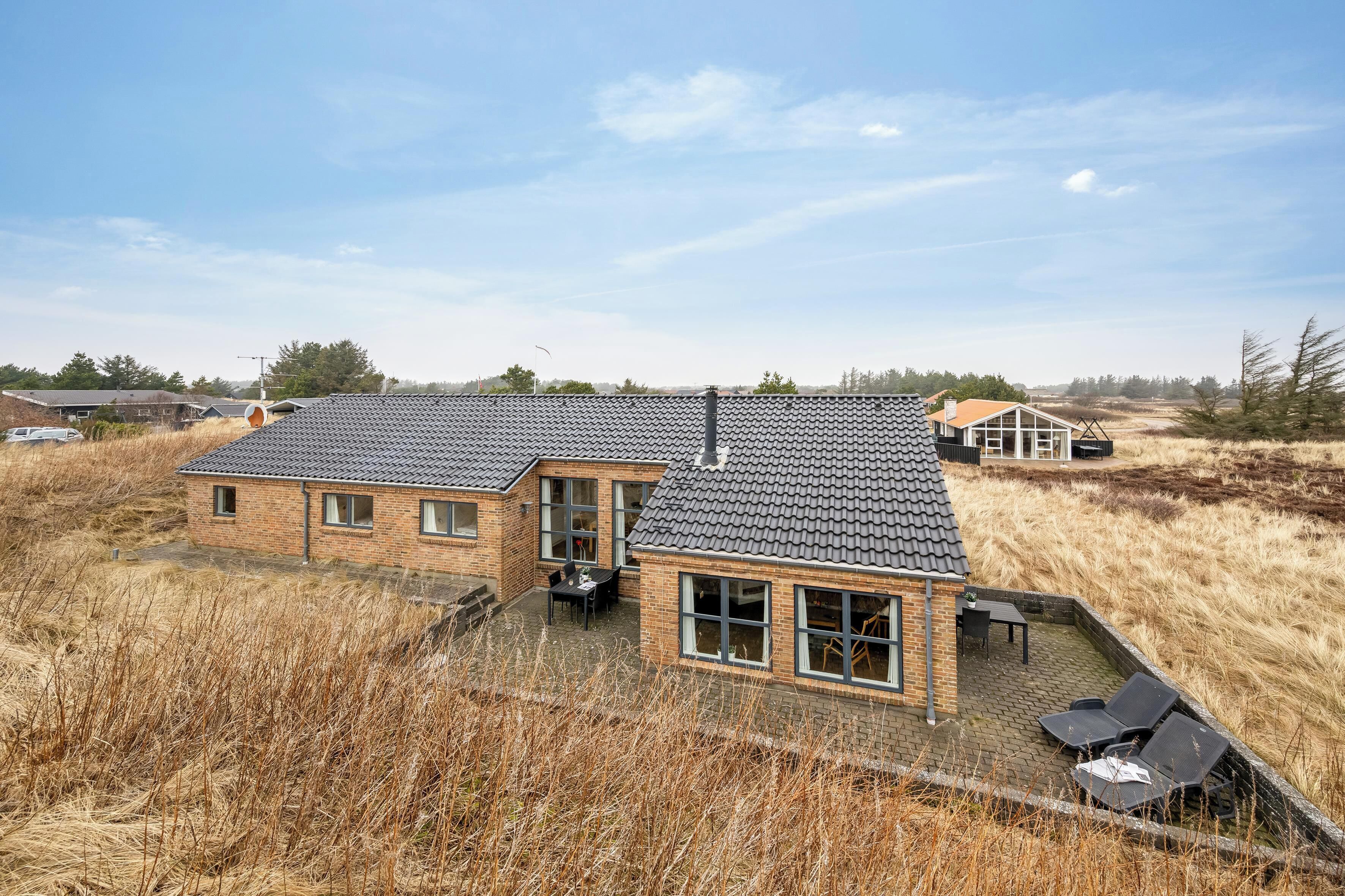 Kaksikerroksinen talo, jossa on tiilikatto, suuret ikkunat ja patio, jossa on ulkokalusteita.