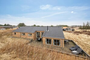Et toetagers hus med tegltag, store vinduer og en patio med udendørs møbler.