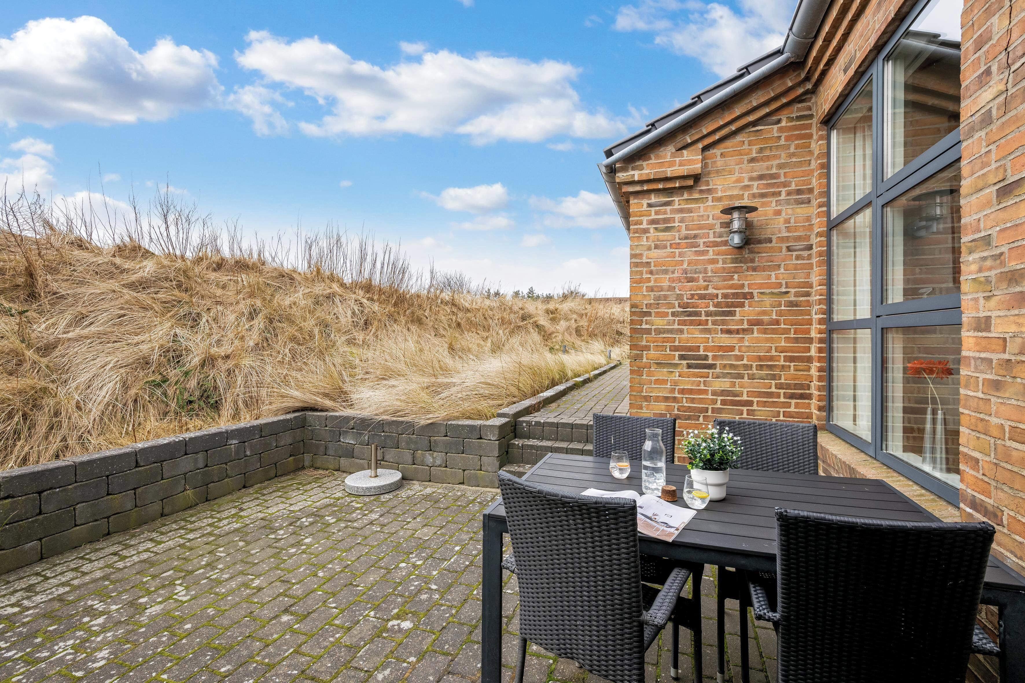 Une terrasse avec un mur en briques, une table avec des chaises, une plante en pot et une bouteille.