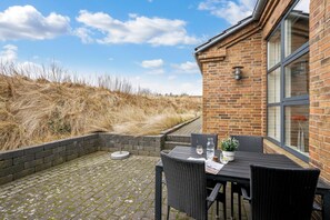 En terrasse med en murstensvæg, et bord med stole, en potteplante og en flaske.