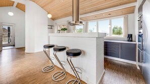 Eine moderne Küche mit Holzbalkendecke, einer zentralen Kochinsel mit Sitzgelegenheiten und großen Fenstern.