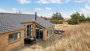 Ein Backsteinhaus mit Ziegeldach, einer Terrasse mit Sitzgelegenheiten und Blick auf die umliegende Landschaft.