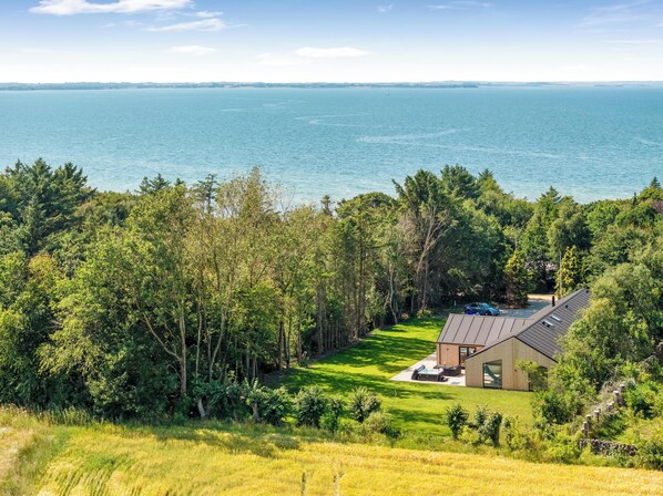 A house with a view of the sea, surrounded by trees and a grassy lawn.