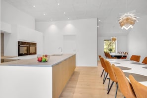 A modern kitchen with a central island, a dining area with a large table and chairs, and a view of the outdoors.