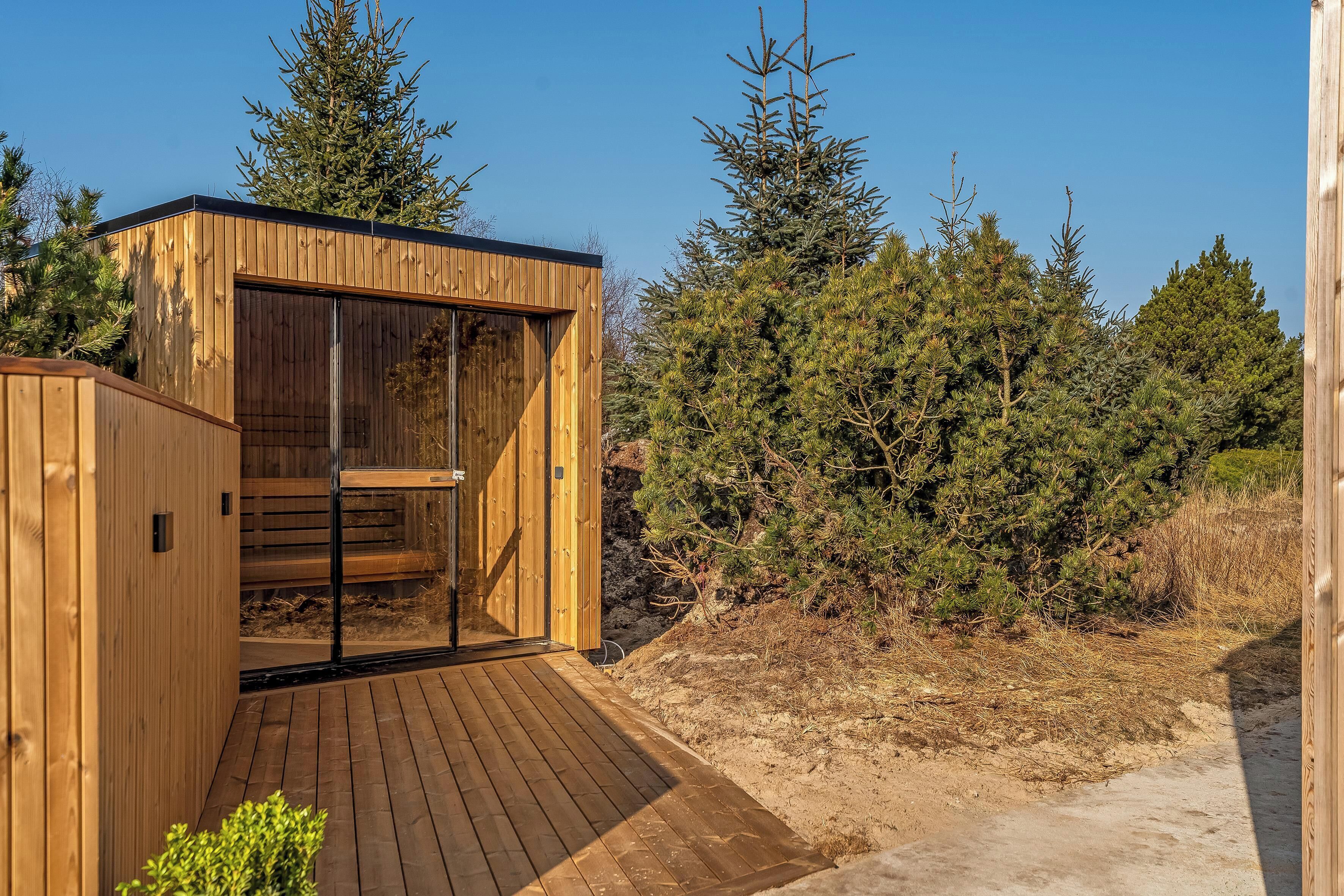 Une structure de sauna en bois dotée d’une porte en verre, entourée d’arbres.