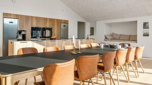 A modern kitchen with a central island, a dining area with a large table and chairs, and a cozy seating area with a sofa. - Luxury holiday home with outdoor hot tub, outdoor sauna and activity room for. (Fjerritslev)