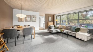 Un salon moderne avec un coin repas, de grandes fenêtres et un plafond en bois.