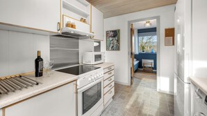 Une cuisine moderne avec des meubles blancs, un four encastré, un micro-ondes et une bouteille de vin.
