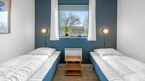 Une chambre avec deux lits, une fenêtre avec des rideaux, un radiateur et des lampes fixées au mur.
