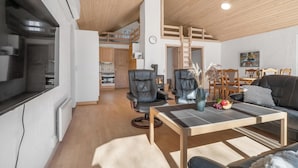 Een moderne woonkamer met een houten plafond, een eethoek en een keuken op de achtergrond.
