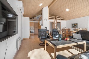 Una sala de estar moderna con techo de madera, un comedor y una cocina al fondo.