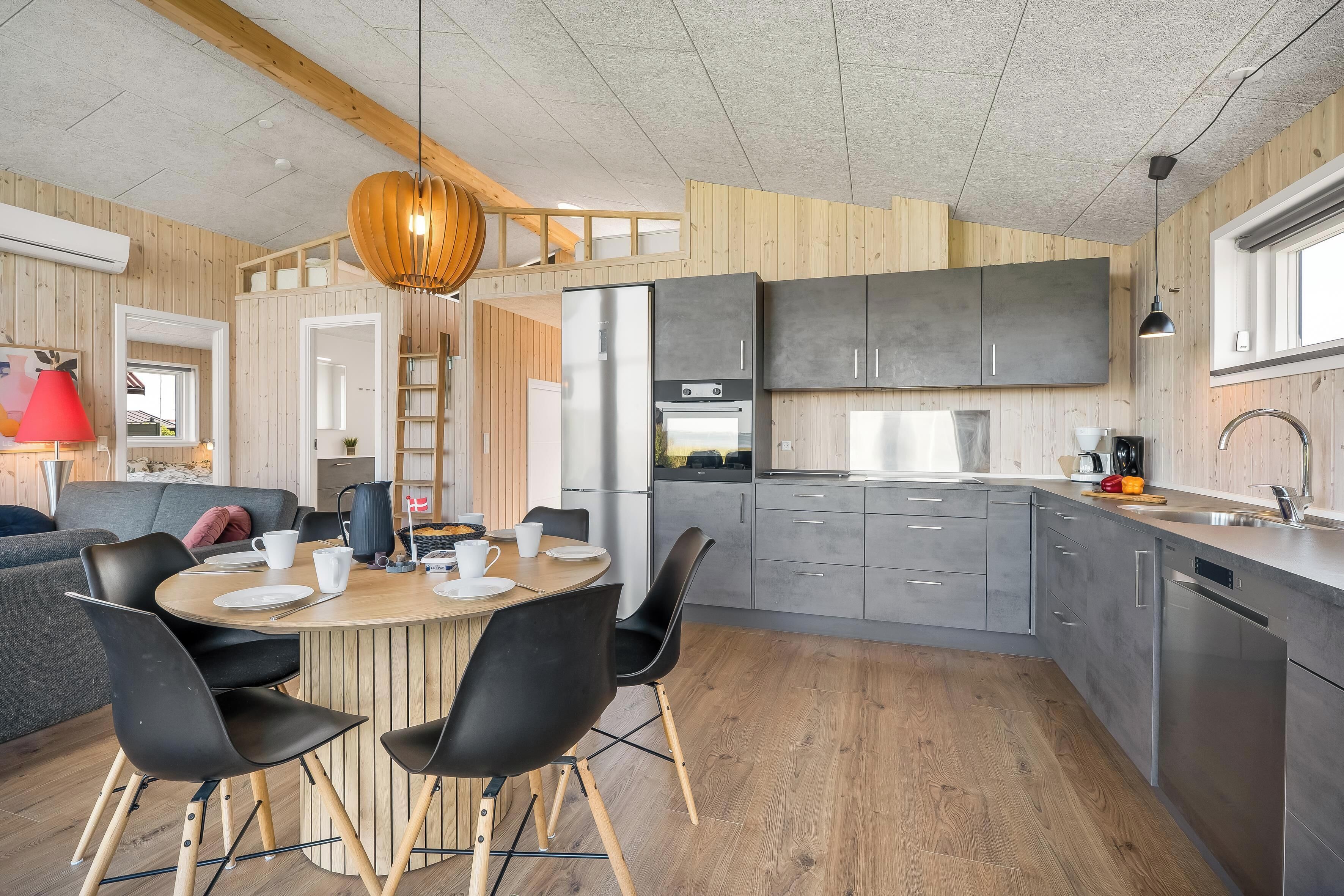 Een moderne keuken met grijze kastjes, een houten eettafel en zwarte stoelen.