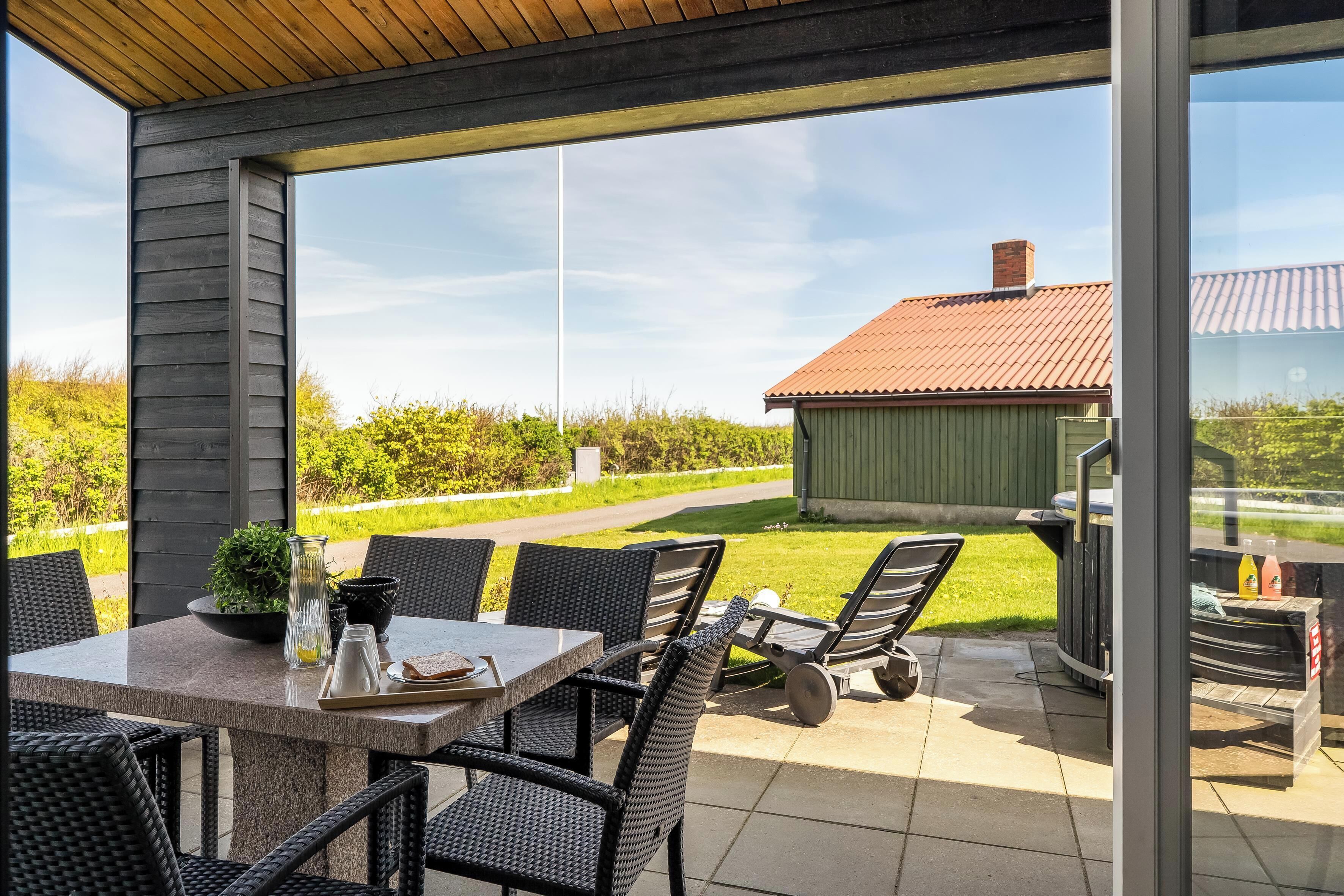 An outdoor patio with a table and chairs, a grill, and a view of a green landscape.