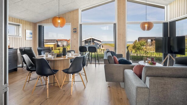 Un intérieur moderne comprenant un coin repas, des canapés et de grandes fenêtres donnant sur l’extérieur.