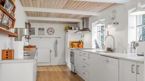 Une cuisine moderne avec des meubles blancs, un plafond en bois et une fenêtre qui laisse entrer la lumière naturelle.