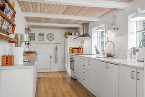 A modern kitchen with white cabinetry, a wooden ceiling, and a window providing natural light.