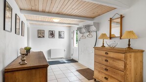 Un couloir avec un plafond en bois, un radiateur, une commode en bois avec des tiroirs, un miroir et des tableaux encadrés accrochés au mur.