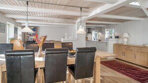 Un espace repas avec une table en bois, des chaises noires, des luminaires suspendus et un tapis rouge.