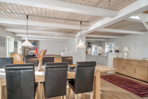 A dining area with a wooden table, black chairs, pendant lights, and a red rug.