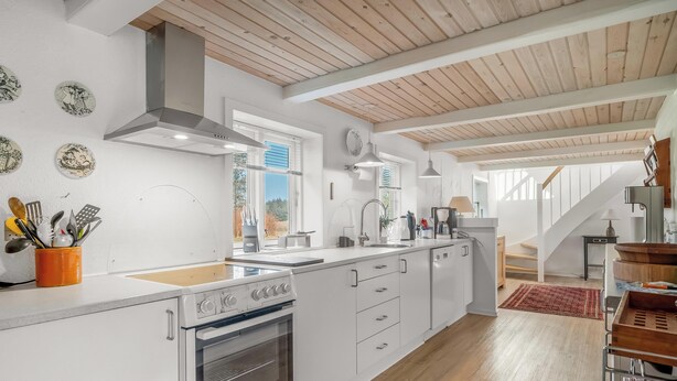 Une cuisine moderne avec des meubles blancs, un four encastré et un plafond en bois.
