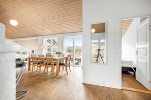Un vaste espace dédié à la salle à manger, avec une table et des chaises en bois, de grandes fenêtres et une vue sur l’extérieur.