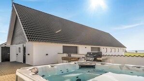 Eine Dachterrasse mit Whirlpool, Grill und einem Gebäude mit geneigtem Dach.