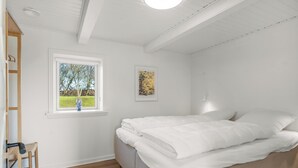 Ein Schlafzimmer mit einem Bett, einem Fenster mit Aussicht, einem Bild an der Wand und einem Holzsessel.