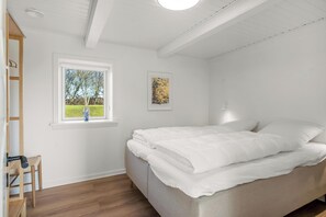 A bedroom with a bed, a window with a view, a painting on the wall, and a wooden chair.