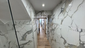 Un pasillo con paredes de mármol y suelo de madera, que conduce a una habitación con una puerta.