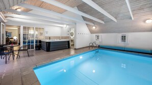 Ein Hallenbad mit Holzbalkendecke, einem Whirlpool und einer Sitzecke mit Tisch und Stühlen.