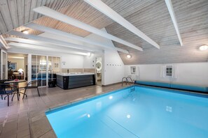 Ein Hallenbad mit Holzbalkendecke, einem Whirlpool und einer Sitzecke mit Tisch und Stühlen.