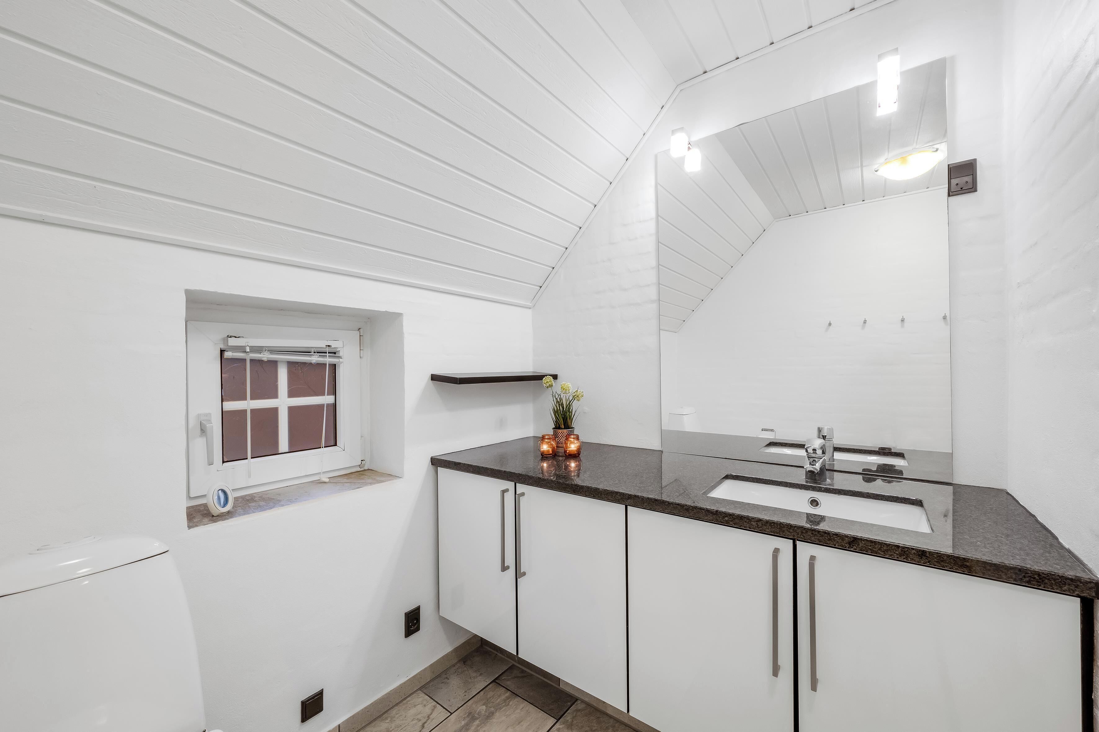 A bathroom with a white vanity, a sink, a mirror, and a window with a view of the outside.
