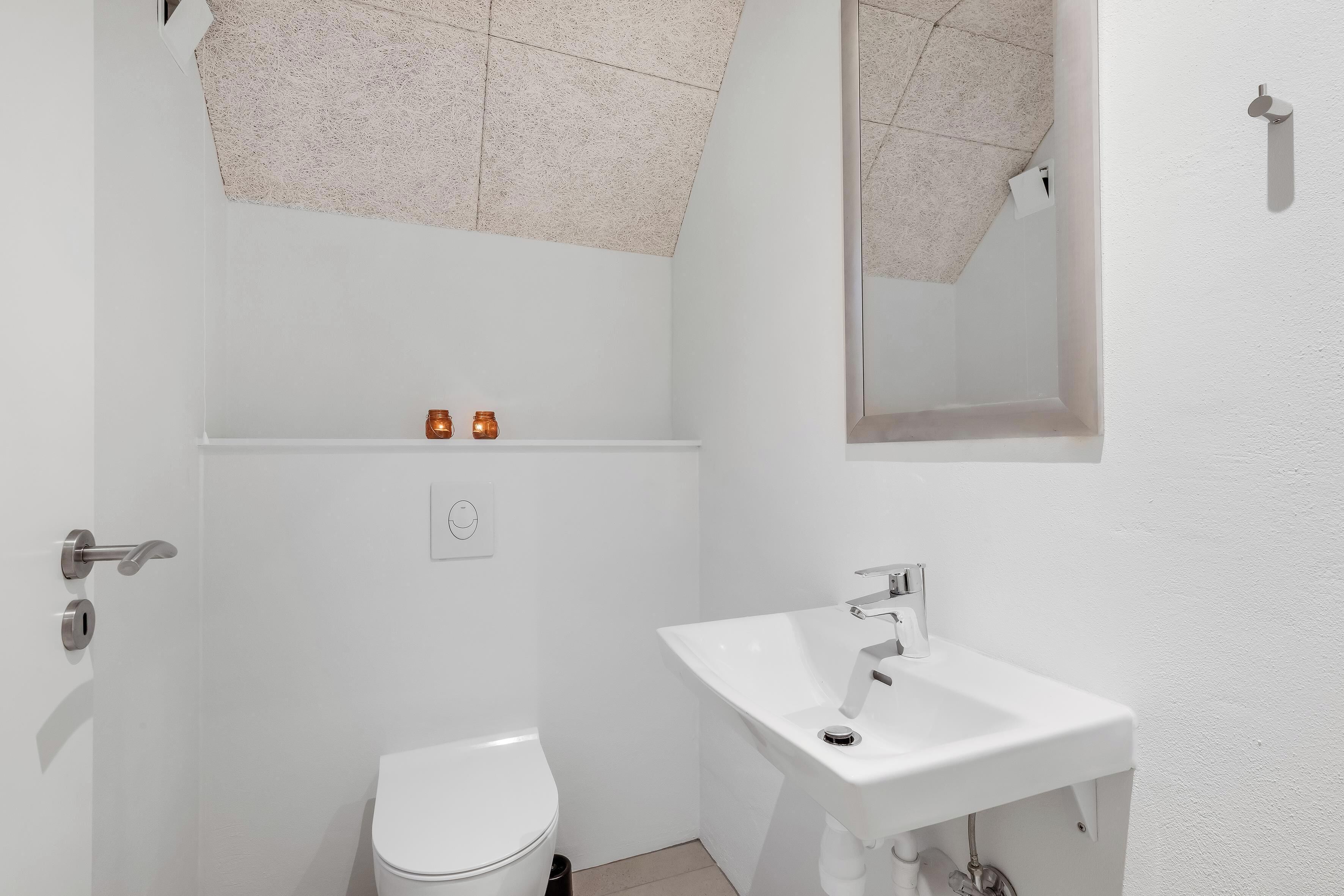 Et lille badeværelse med toilet, håndvask og spejl.