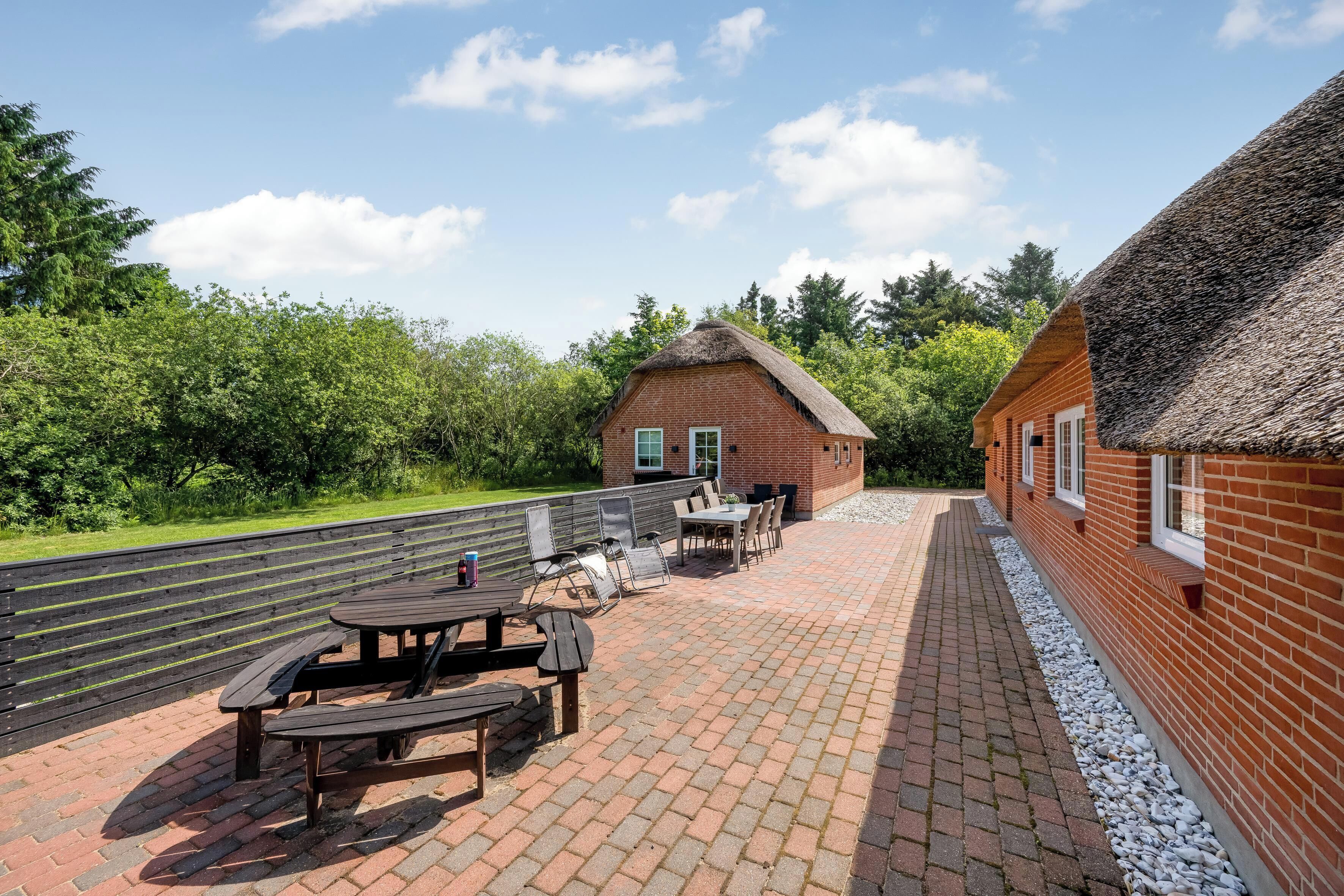 A patio area with a brick floor, wooden tables and benches, and a thatched-roof building.