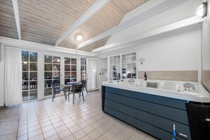 Une cuisine moderne dotée d’un grand îlot central, d’un coin repas avec des chaises et d’une vue dégagée grâce à des portes vitrées.