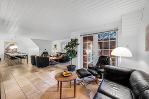 Ein großzügiger Wohnbereich mit Esstisch, Ledersofas, einem Couchtisch mit Obst und einem großen Fenster mit Aussicht.