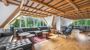 Ein großzügiger Loft-Raum mit hohen Decken, großen Fenstern und verschiedenen Sitzgelegenheiten, darunter Sofas und ein Relaxsessel.