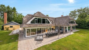 Ein Haus mit einer großen Terrasse, Sitzgelegenheiten im Freien und einem Strohdach.