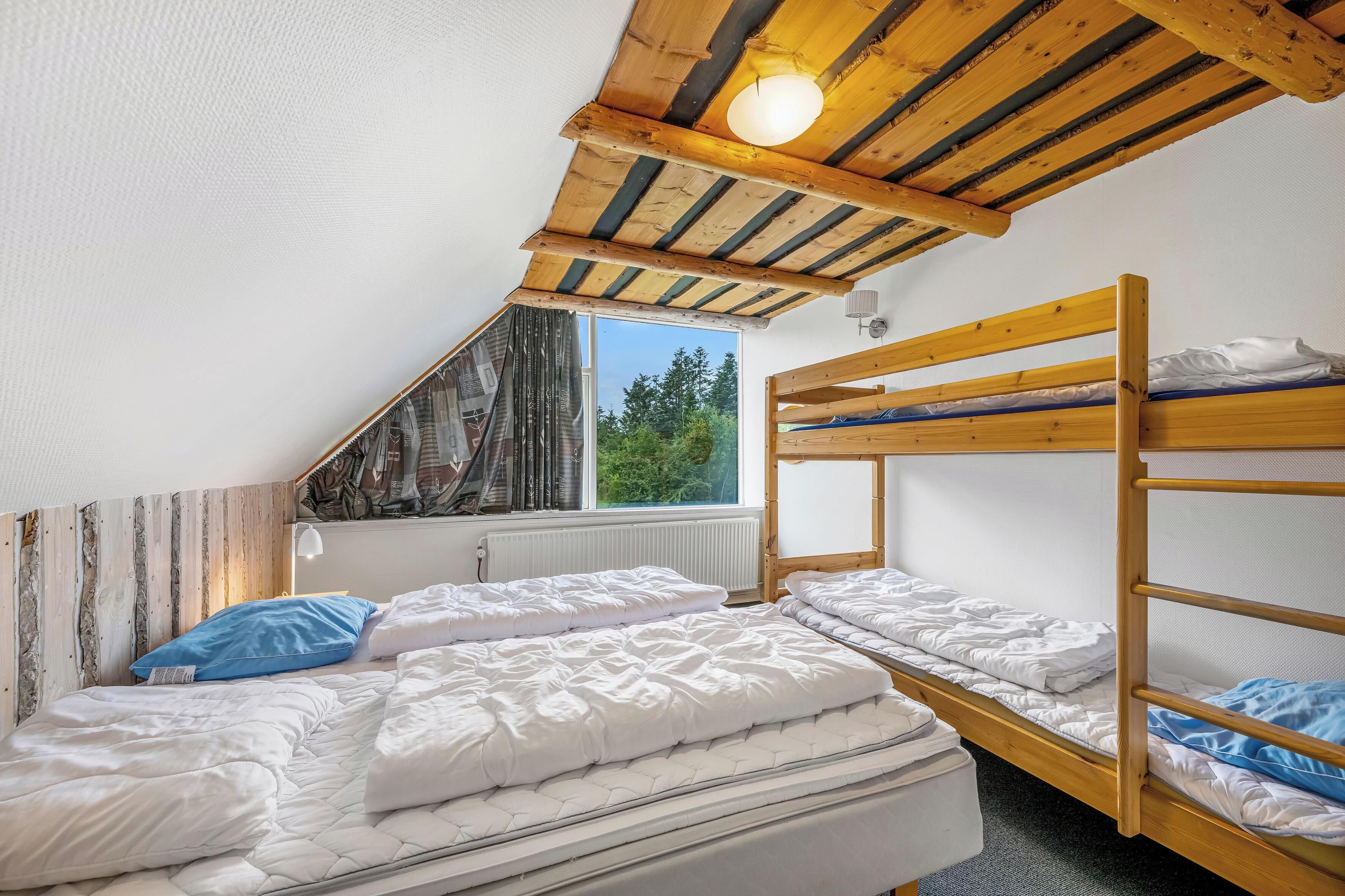 A dormitory room with bunk beds, a sloped ceiling, a window with a view of trees, and a radiator.