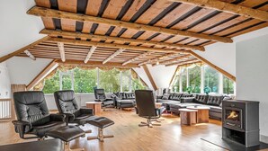 Ein großzügiges Loft mit Holzbalkendecke, Ledersofas, einem Kamin und großen Fenstern.