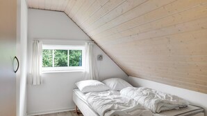 Ein Schlafzimmer mit schrägem Dach, einem Einzelbett, einem Fenster mit Vorhängen und einer Wandleuchte.